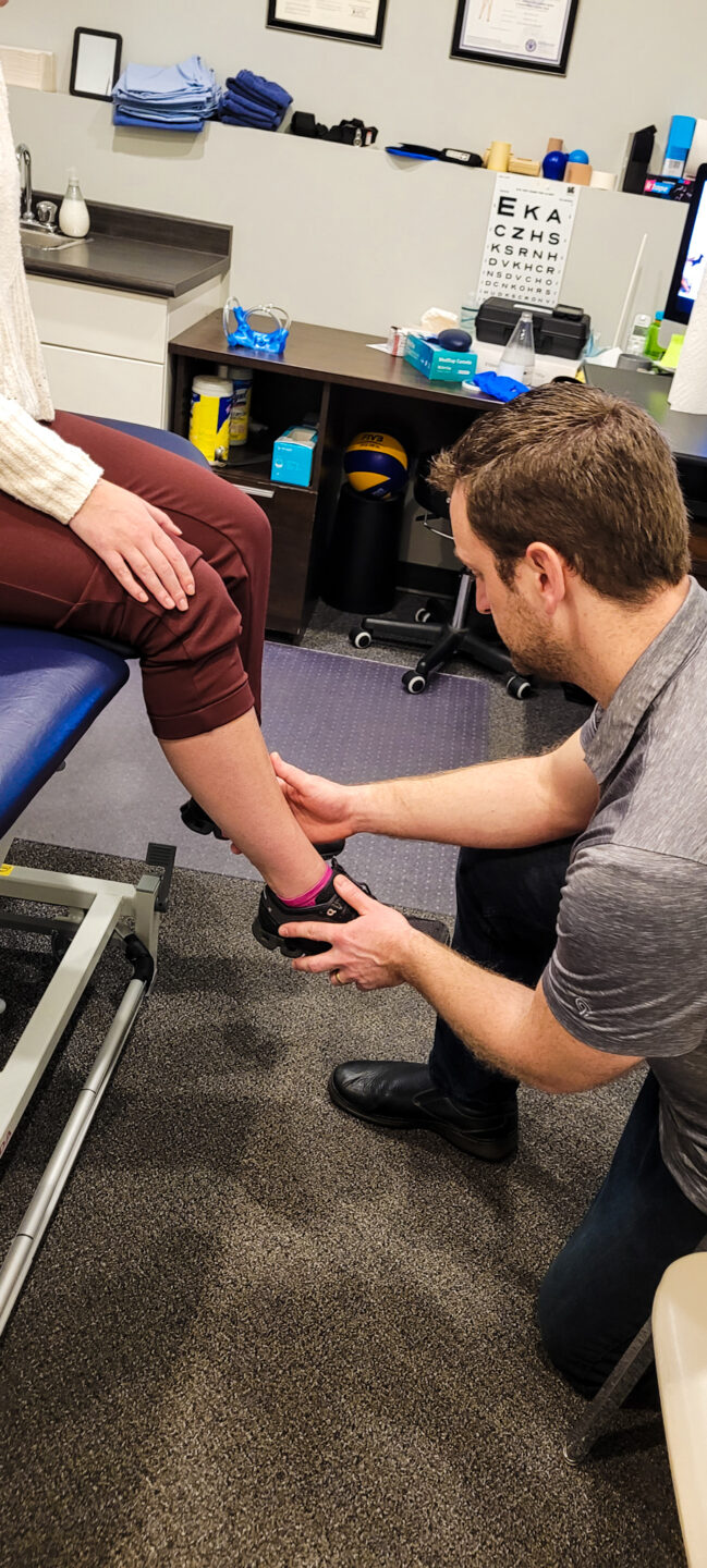 A Physiotherapist holding a clients lower leg in hand assessing for shin splints